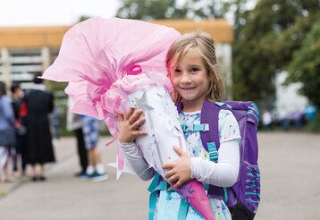Mädchen steht mit einer großen Schultüte auf dem Schulhof, im Hintergrund eine Gruppe von Leuten