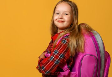 Mädchen mit kariertem Hemd und pinkem Tornister vor orangem Hintergrund