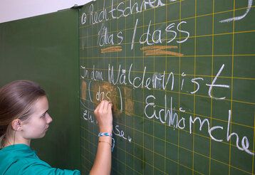 Mädchen schreibt mit Kreide an eine  Schultafel
