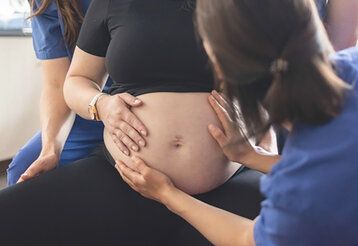 Hebamme tastet den Bauch einer schwangeren Frau ab