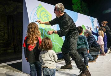 Martin Baltscheit malt auf eine große Papierplane, andere Erwachsene und Kinder malen mit oder gucken zu