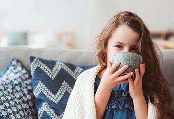 Kind auf dem Sofa trinkt aus einer Schale