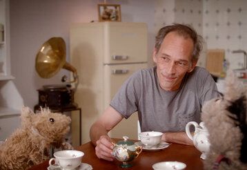 Mann sitzt mit Stofftieren am Kaffeetisch