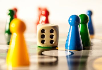 Mensch-ärgere-dich-nicht-Figuren und ein Würfel auf einem Spielbrett