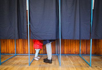 Menschen wählen in Wahlkabine mit Kind