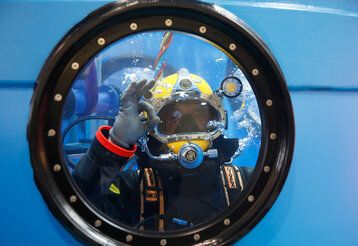 durch ein Bullauge sieht man einen Taucher, der ein Handzeichen gibt, dass alles perfekt ist