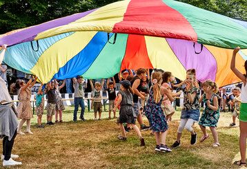 Kinder spielen auf einer Wiese und schwingen einen großen runden Stoff