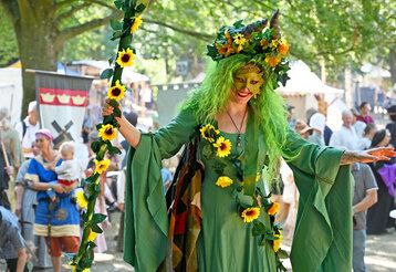 Eine Frau ist als Fee oder Waldgeist verkleidet, im Hintergrund Mittelaltermarkt mit Besucher:innen