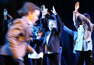 Eine Gruppe Kinder tanzt eine Choreographie und trägt dabei Anzüge.