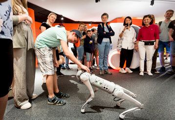Gruppe von Museumsbesuchern steht zusammen, ein Junge streichelt einen Roboter-Hund