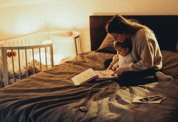 Mutter sitzt mit Baby auf dem Bett und guckt sich ein Buch an