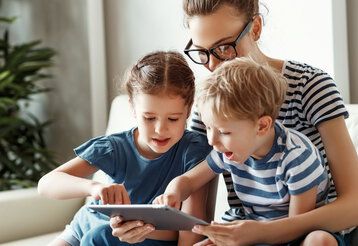 junge Mutter mit kleinem Sohn und Tochter, die auf dem Sofa sitzen und auf das Tablet schauen