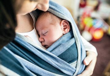Mutter trägt ihr Baby im Tragetuch, Perspektive von oben, Hintergrund unscharf