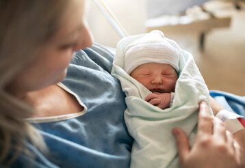 Junge Mutter hält ihr neugeborenes Baby im Arm