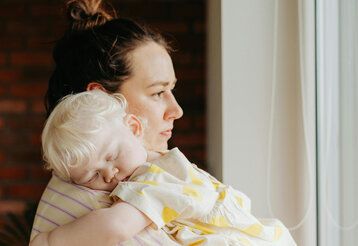Mutter guckt nachdenklich und hat ein Baby auf dem Arm