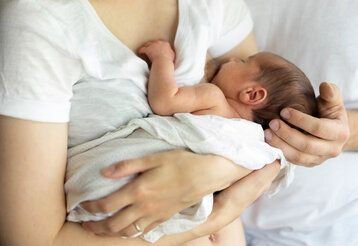 Mutter stillt Baby, Hand des Vaters hält den Kopf des Babys