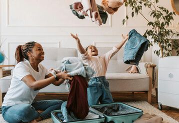 Mutter und Kind packen Koffer, das Kind schmeißt Anziehsachen in die Luft