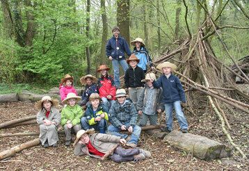 Gruppenfot von Kindern im Wald vor einer selbstgebauten Holzhütte