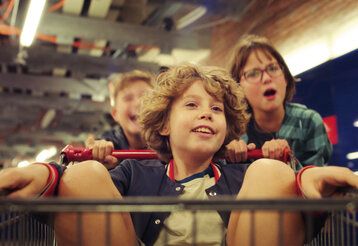 Ein Junge sitzt in einem Einkaufswagen und wird von zwei anderen Kindern geschoben