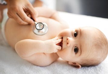 Ein Baby liegt auf dem Rücken und wird mit einem Stethoskop abgehört