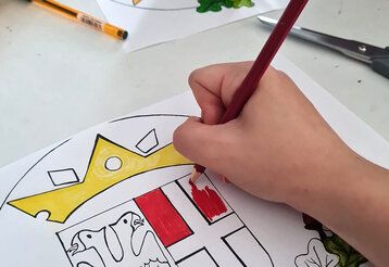 Kinderhand mit Buntstift, die eine Malvorlage des Neusser Wappens ausmalt