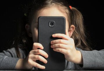 ein mädchen hält sich ein großes schwarzes Smartphone vors Gesicht