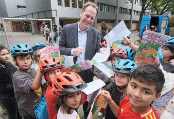Oberbürgermeister Keller steht auf einem Schulhof und ist umringt von Grundschulkindern, die Malbücher in den Händen halten