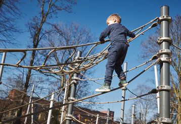 Junge klettert auf einer Seilpyramide auf einem Spielplatz in Pempelfort