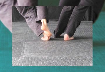 Zwei Menschen, von denen nur die nackten Füsse und die Hosenbeine zu sehen sind, tanzen auf einem Fliesenboden.