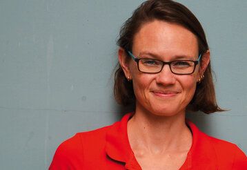 Porträt von Inke Hummel in rotem Shirt vor grauer Wand