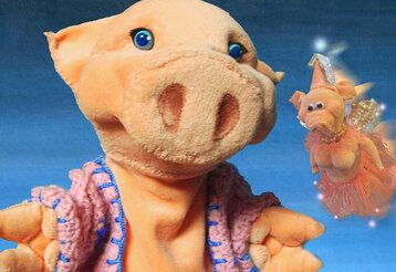 großes Plüschschwein mit rosa Häkelweste im Vordergrund, daneben fliegt eine kleine Schweine-Fee, der Hintergrund ist blau
