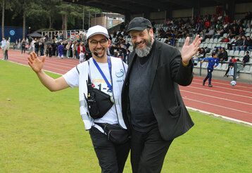 Rabbi Malinsky und Veranstaltungsleiter Redouan Aoulad Ali stehen Arm in Arm, im Hintergrund ein Sportplatz mit einer Tribüne mit Publikum