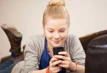 Mädchen liegt auf einer Couch und guckt aufs Smartphone