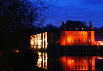 Schloss Dyck bei Nacht, rot angestrahlt, Spiegelung im Wassergraben