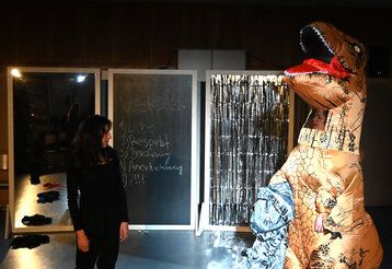 Zwei Frauen auf einer Bühne, ein davon trägt ein Dinosaurier-Kostüm