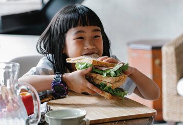 asiatisches Mädchen beißt in ein sehr großes Sandwich