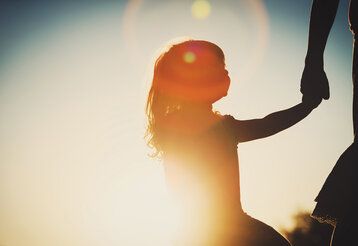 Kind an der Hand der Mutter, im Gegenlicht fotografiert mit Sonnenflecken