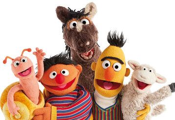 Ernie und Bert und weitere Figuren der Sesamstraße winken in die Kamera