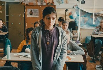 ein Mädchen steht in einer Schulklasse und guckt traurig