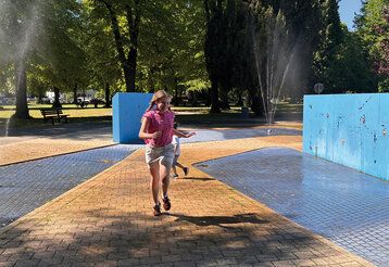 ein Mädchen rennt zwischen Wasserfontänen her auf dem Spielplatz Alter Bilker Friedhof