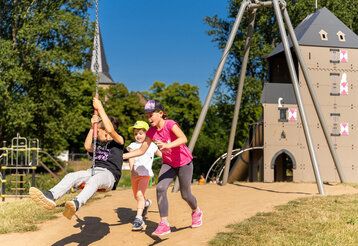 Drei Kinder spielen auf einem Spielplatz mit Seilbahn im Landschaftspark in Monheim am Rhein
