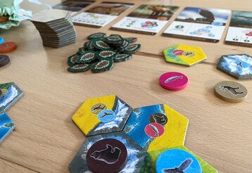 Spielkarten und -plättchen vom Spiel Cascadia liegen auf einem Tisch
