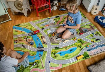 Zwei Kinder spielen mit Autos auf dem Straßenteppich der Libelle