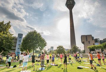 Sport im Park-Kurs mit Teilnehmenden, die auf der Wiese vor dem Rheinturm turnen