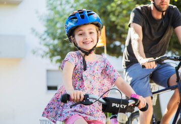 Mädchen mit Helm fährt Fahrrad, im Hintergrund ein Mann auf einem Fahrrad