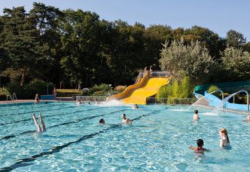 Freibad mit gelber Wasserrutsche, im Hintergund Bäume