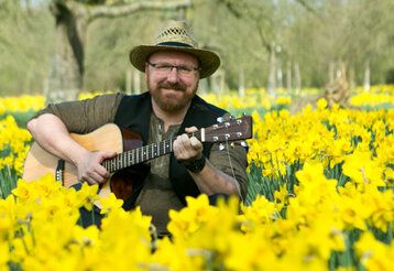 Stefan Strohhut sitzt mit seiner Gitarre in einem Narzissenfeld