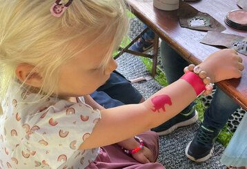 Kleines Mädchen mit einem roten Mammut-Tattoo auf dem Arm