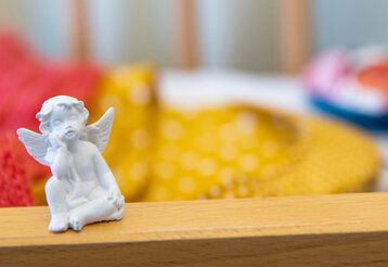 Eine kleine Engelsfigur, im Hintergrund ein leeres Babybett