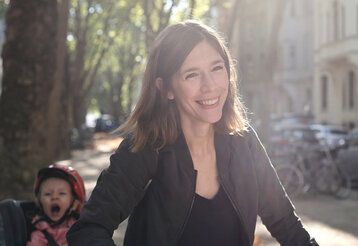 Junge Frau auf einer sommerlichen Straße, Kind im Fahrradkindersitz hinter ihr